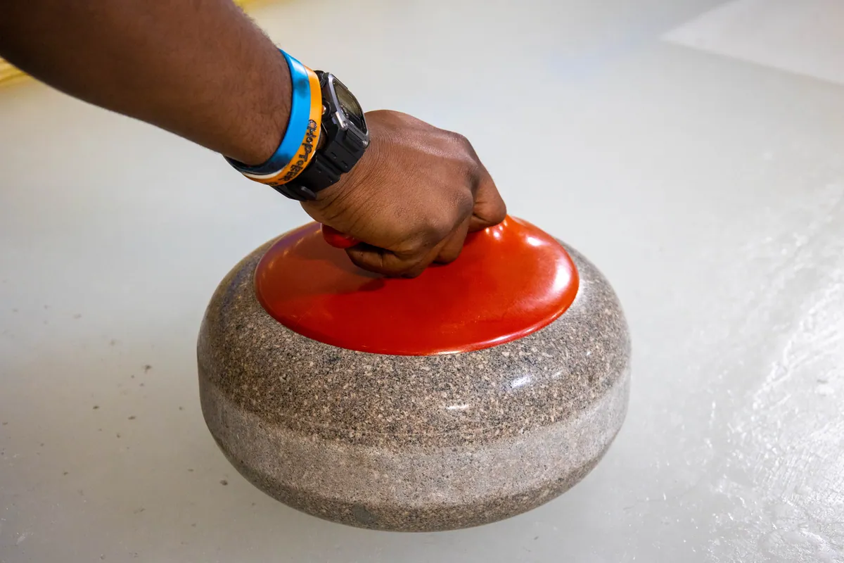 A hand set on the handle of a curling stone